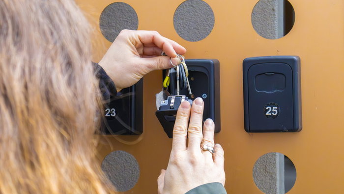 Property owner placing a key in a self check-in lockbox outside a holiday rental apartment in Spain.