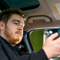 Young driver checking his phone while sitting inside a parked car.