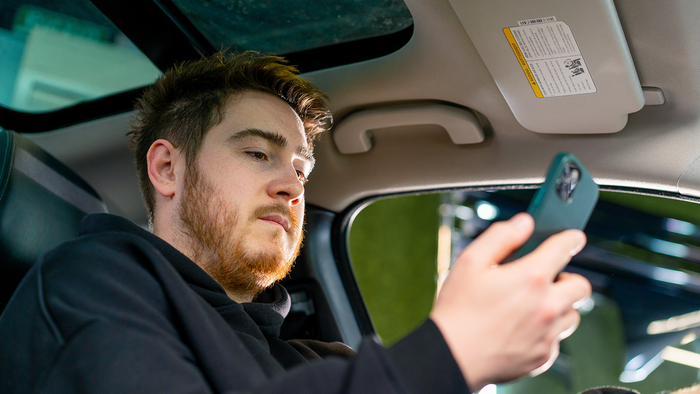 Young driver checking his phone while sitting inside a parked car.