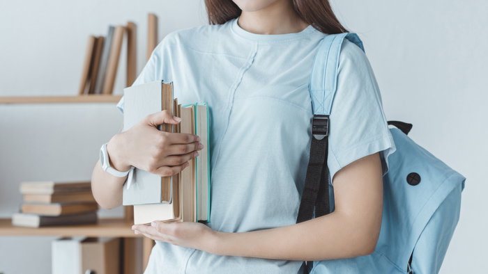 Young girl student holding her books with a blue backpack on