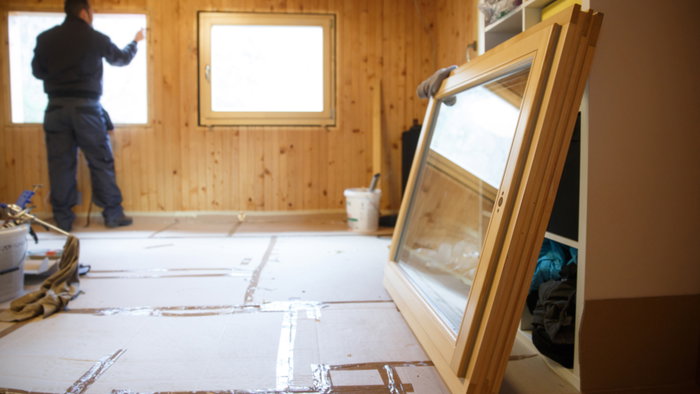 Worker in the backgournd in a Wooden house installing wooden windows for sustainable living & energy savings