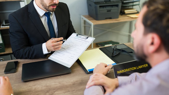 An immigration lawyer discusses a residence application with foreign clients during a consultation on family reunification and immigration procedures.
