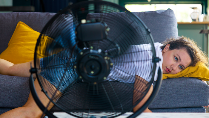 Woman lying on the sofa with an electric fan on cooling off during a heat wave