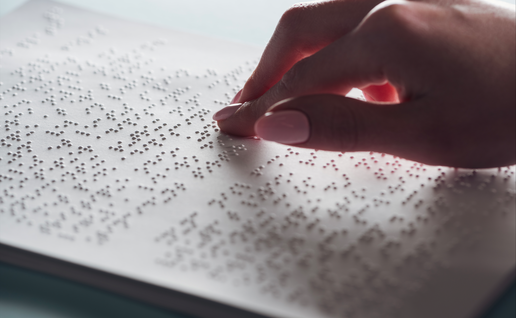 cropped view of young woman reading braille text on white paper