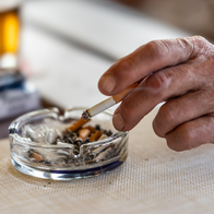 A mans hand holding a cigarette over an ashtray