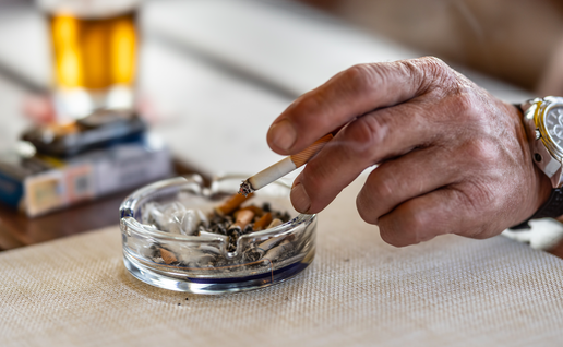 A mans hand holding a cigarette over an ashtray