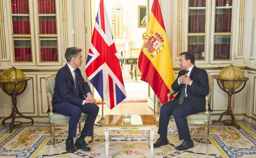 Spanish and UK foreign Ministers sitting down during a meeting in Madrid with both Spanish and UK flags in the backgrounds