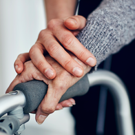 An elder woman's hand on a zimmer frame with a younger hand on top of hers