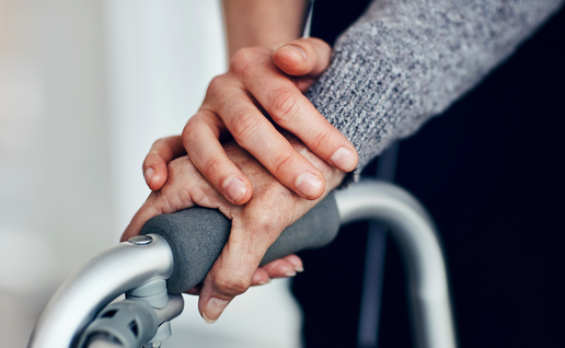 An elder woman's hand on a zimmer frame with a younger hand on top of hers