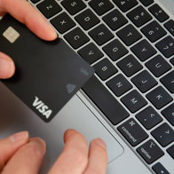 A Visa payment card held above a laptop keyboard while booking travel online.