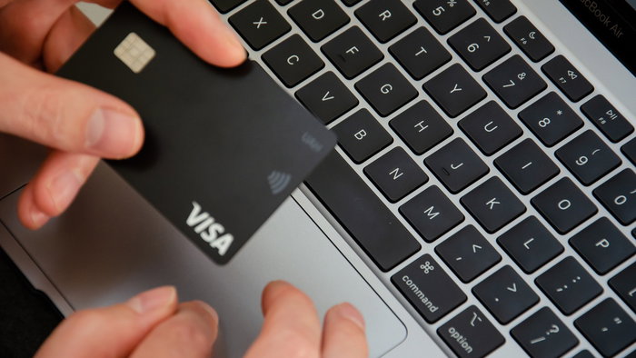 A Visa payment card held above a laptop keyboard while booking travel online.