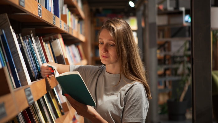 Woman browsing books in a second hand bookshop as AI firms reportedly buy out of print titles for data.