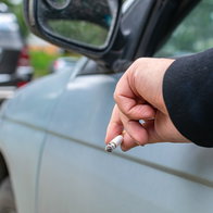 Driver holding a lit cigarette out of a car window while stopped in traffic.