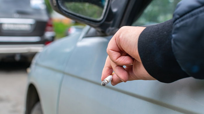 Driver holding a lit cigarette out of a car window while stopped in traffic.