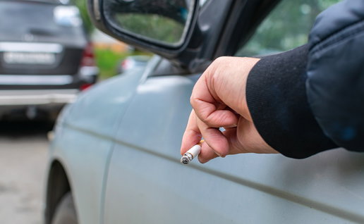 Driver holding a lit cigarette out of a car window while stopped in traffic.