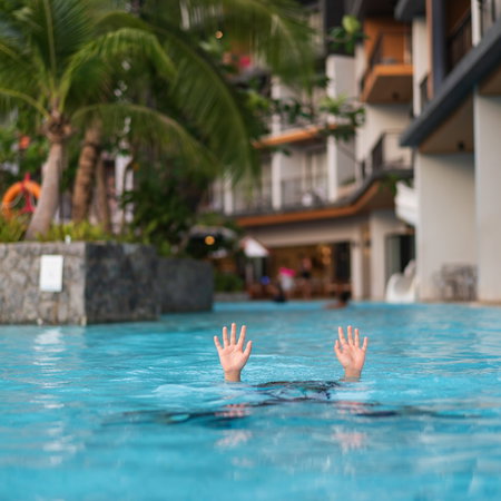 Child struggling in a swimming pool with only their hands visible above the water.