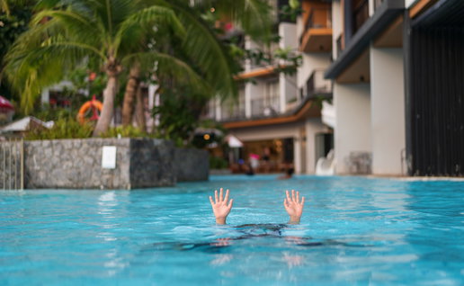 Child struggling in a swimming pool with only their hands visible above the water.