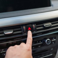 A driver presses the hazard warning light button inside a car, highlighting the correct use of emergency flashers on Spanish roads.
