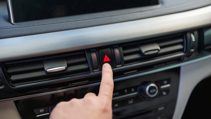 A driver presses the hazard warning light button inside a car, highlighting the correct use of emergency flashers on Spanish roads.