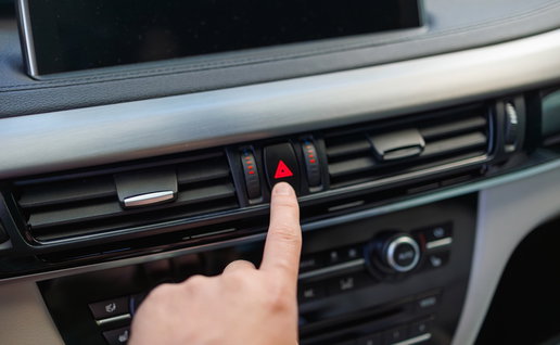 A driver presses the hazard warning light button inside a car, highlighting the correct use of emergency flashers on Spanish roads.