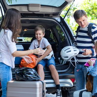 Family loading luggage into the boot of a car before setting off on a summer road trip.