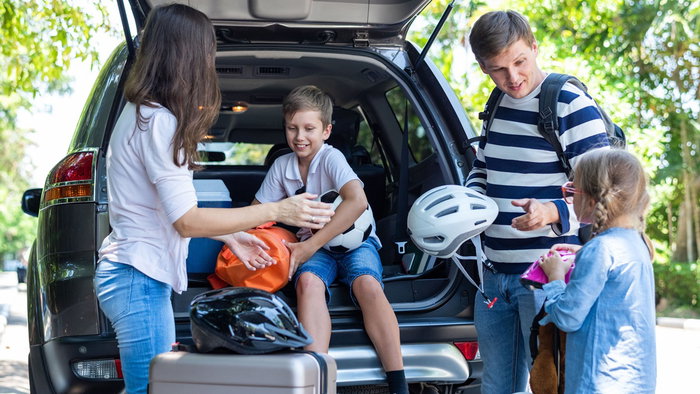 Family loading luggage into the boot of a car before setting off on a summer road trip.