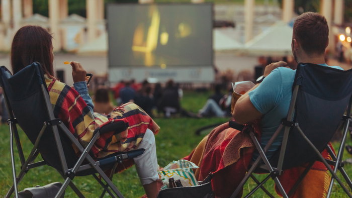 couple sitting in camp-chairs in city park looking movie outdoors at open air cinema lifestyle