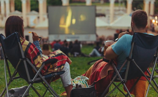 couple sitting in camp-chairs in city park looking movie outdoors at open air cinema lifestyle