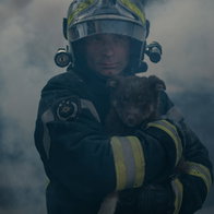Firefighter coming through smoke carrying a small dog