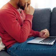 A frustrated man sitting on a sofa writing on his laptop