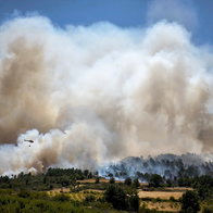 A helicopter throwing water over a rising cloud of smoke from a forest fire in Portugal