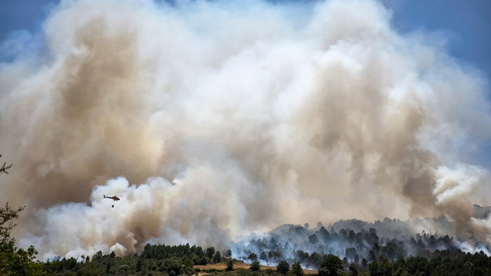 A helicopter throwing water over a rising cloud of smoke from a forest fire in Portugal