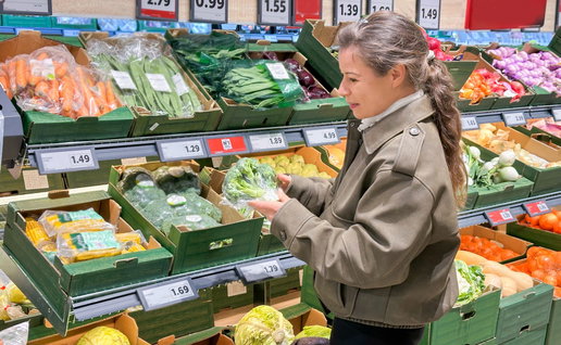 A woman choosing some vegetables off of a supermarket shelf