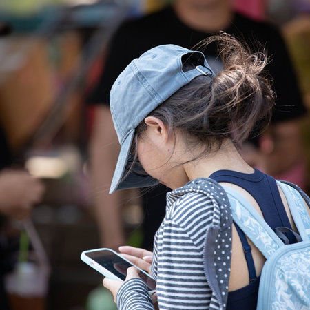 Woman with rucksack on her back with a cap on her head and looking at a mobile phone