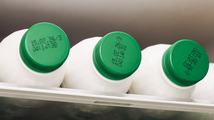 Fresh milk on a refrigerator shelf with expiration dates visible on the lids