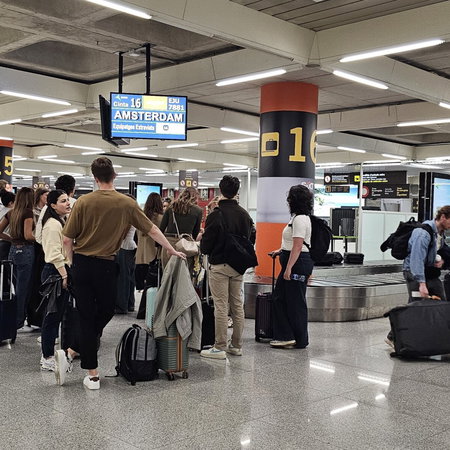 Passengers wait with suitcases at baggage reclaim carousel.