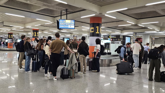 Passengers wait with suitcases at baggage reclaim carousel.