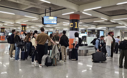 Passengers wait with suitcases at baggage reclaim carousel.