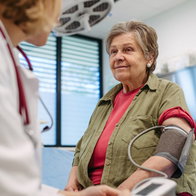A doctor checking an older woman's blood pressure with a digital monitor during a routine cardiovascular health checkup in a medical clinic.