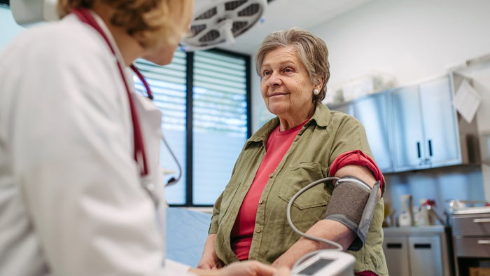 A doctor checking an older woman's blood pressure with a digital monitor during a routine cardiovascular health checkup in a medical clinic.