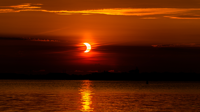 An eclipse occurring on the horizon over the sea between the clouds.