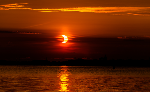 An eclipse occurring on the horizon over the sea between the clouds.