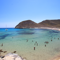 View from above of the Playazo beach in Rodalquilar, Níjar, whilst people swim in the water and sunbathe on the sand.