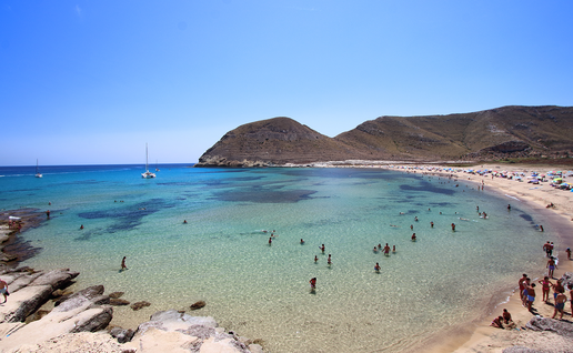 View from above of the Playazo beach in Rodalquilar, Níjar, whilst people swim in the water and sunbathe on the sand.