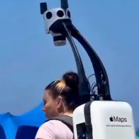 Woman wears Apple Maps backpack to map coastal street.