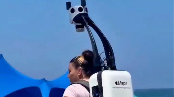 Woman wears Apple Maps backpack to map coastal street.