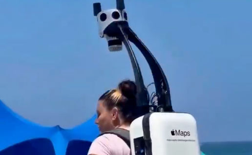 Woman wears Apple Maps backpack to map coastal street.