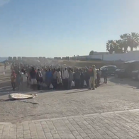 Migrants line up at Playa del Trampolín in Ceuta next to police officers ready to be transferred to shelters.