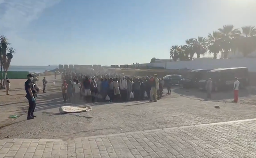 Migrants line up at Playa del Trampolín in Ceuta next to police officers ready to be transferred to shelters.