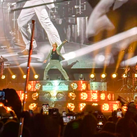 David Bisbal singing on stage at Cooltural Fest, Almería, with the band and lighting rig behind him and the crowd filming on phones in front.